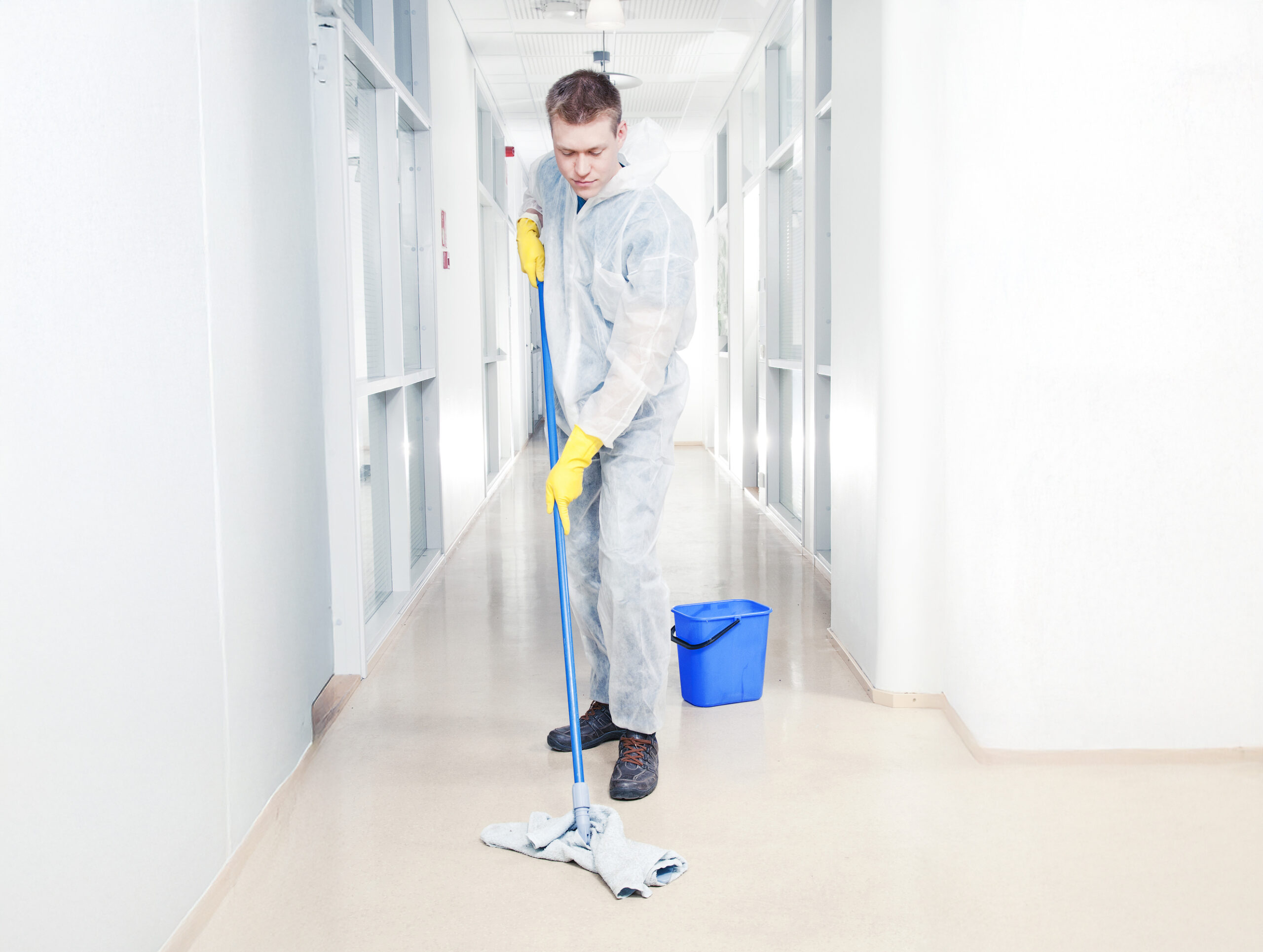 Man cleaning office wearing protective overalls with a mop