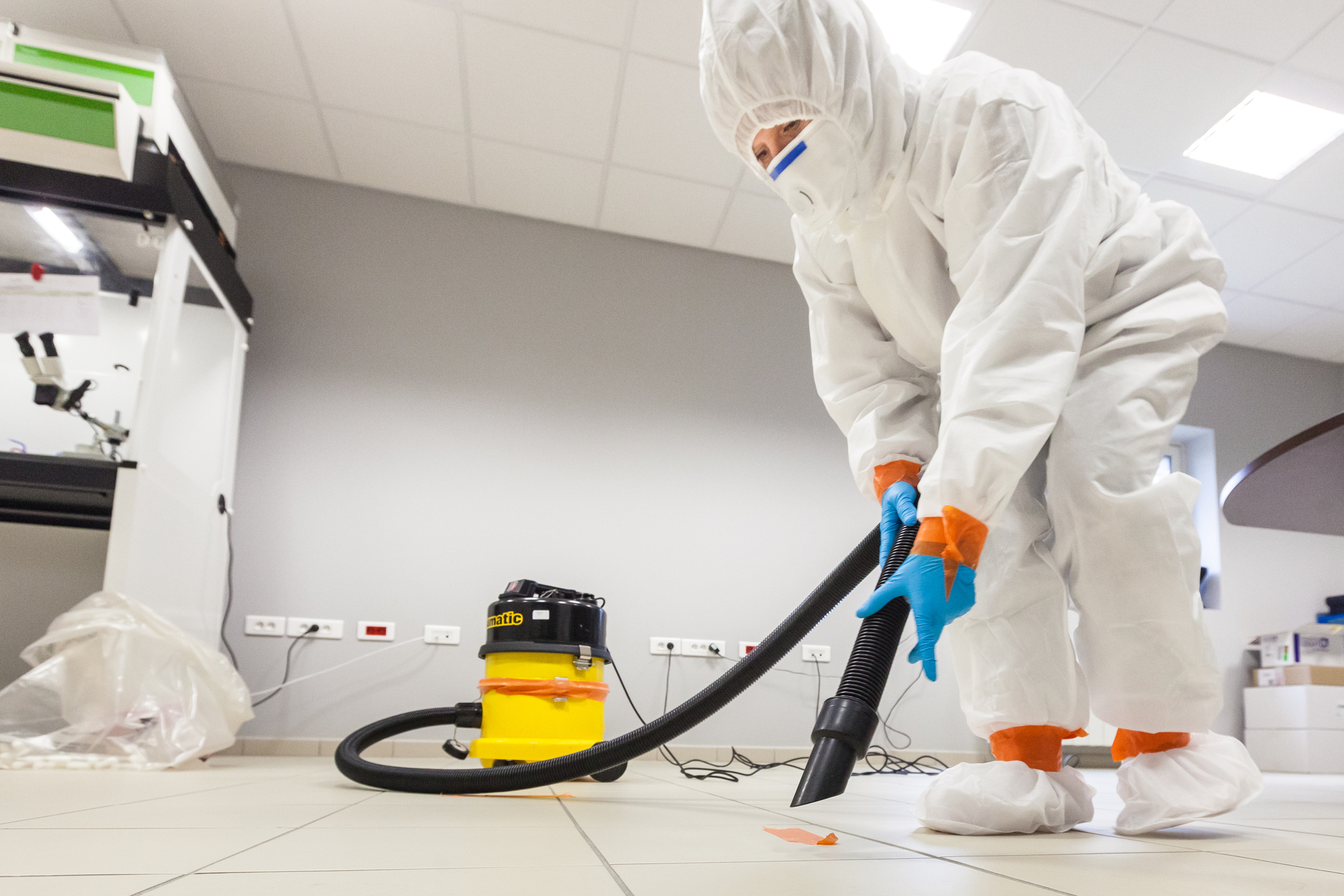 A person in a white suit and protective gear operates a vacuum cleaner.